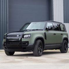 a green land rover parked in front of a building with a garage door behind it