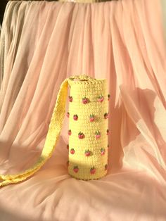 a yellow crocheted bag sitting on top of a pink bed sheet with a ribbon around it