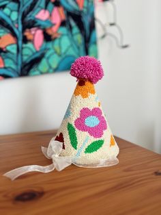 a knitted party hat with flowers on it sitting on top of a wooden table