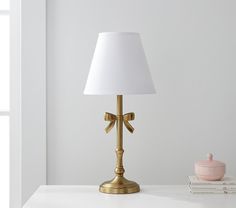 a gold lamp with a white shade sitting on top of a table next to some books