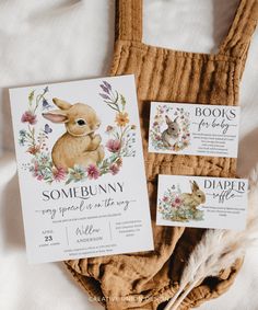 some bunny cards are laying on top of a bed next to an envelope and feather