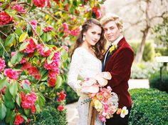 a man and woman standing next to each other in front of flowers