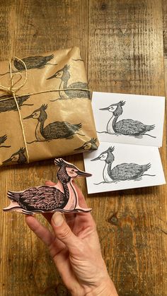 a hand holding a bird ornament next to two envelopes with birds on them