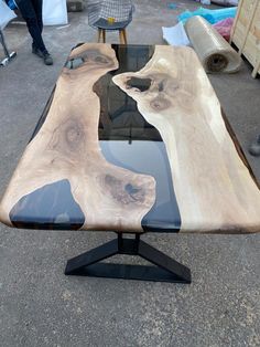 a table made out of wood and glass with black metal legs on the top, in an outdoor area