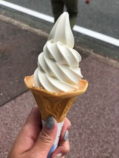 a hand holding an ice cream cone on the street