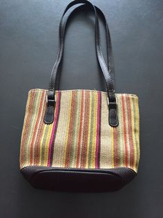 This cute purse is made by Liz Claiborne and has multi colors of tan, beige, brown, yellow, orange, green and pink basket weave fabric with a brown faux leather trim, bottom, and straps. The compartment has a flap closure with magnetic snap and opens to a bright pink fabric lined inside and one small side zippered pocket. The double straps each measure 22 inches in total length (drop length from shoulder 11 inches).  The purse measures 7 inches in length by 8 inches in width and is in good condition with only a few not noticeable marks . Retro Brown Shoulder Bag For Vacation, Casual Multicolor Fabric Shoulder Bag, Brown Fabric Shoulder Bag For Travel, Casual Brown Fabric Shoulder Bag, Casual Brown Fabric Bag, Handwoven Multicolor Leather Bags, Multicolor Woven Leather Rectangular Bag, Eco-friendly Multicolor Straw Bag With Braided Handles, Eco-friendly Multicolor Woven Shoulder Bag