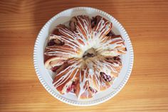 a white plate topped with a bundt cake covered in icing on top of a wooden table