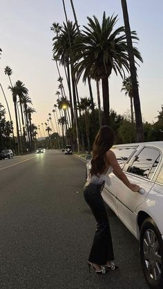 a woman riding a skateboard next to a white car on a street with palm trees