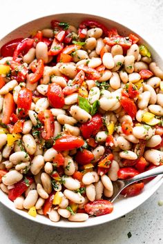 a white bowl filled with beans, tomatoes and green herbs on top of a table