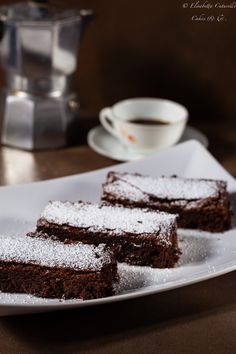 three pieces of chocolate cake on a plate with powdered sugar and coffee in the background