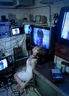 a woman sitting on the floor in front of televisions