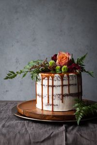 a cake with flowers and greenery on top is sitting on a wooden platter