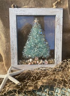 a christmas tree in a frame with shells and starfish on the table next to it