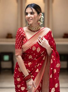 a woman in a red and gold sari with jewelry on her neck, smiling at the camera