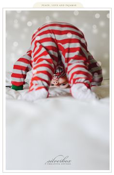 a baby is dressed in red and white striped pajamas while laying down on the bed