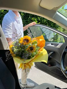 a woman standing next to a car holding a bouquet of sunflowers