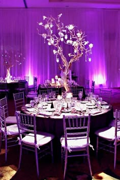 the table is set up for an event with purple lighting and white linens on the walls