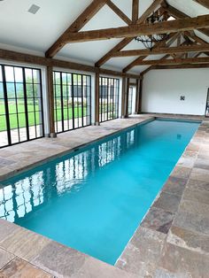 an indoor swimming pool in a house with stone flooring and windows overlooking the lawn