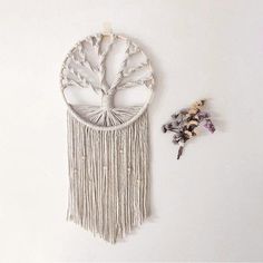 a white wall hanging with a tree of life on it and dried flowers next to it