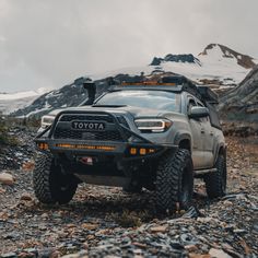 a toyota truck is parked on the side of a rocky road in front of some mountains