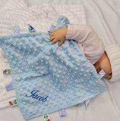 a baby laying on top of a bed under a blue blanket with name written on it