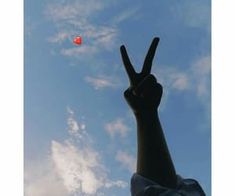 a hand making the peace sign with an orange ball in the sky behind it on a sunny day