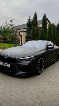 a black car parked in front of a house on a brick driveway next to trees