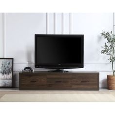 a flat screen tv sitting on top of a wooden entertainment center next to a potted plant