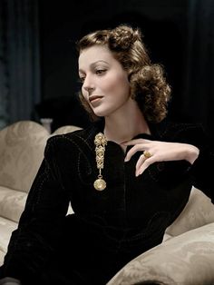 a woman sitting on top of a couch wearing a black dress and holding a necklace