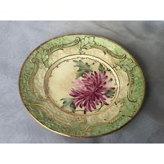 a green and gold plate with a pink flower on it