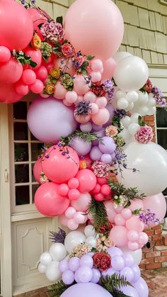 a bunch of balloons that are hanging from the side of a building with flowers on them