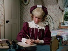 a woman sitting at a table writing in a book with a pen and paper on it