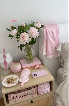 pink flowers in a vase on a small table next to a bed with pillows and blankets