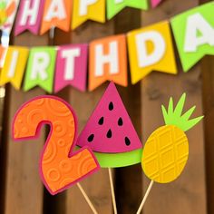 a birthday cake with pineapples and watermelon on sticks in front of a happy birthday banner