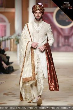 a man walking down the runway wearing a white outfit with red and gold details on it