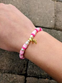 a person wearing a pink and white bracelet with a gold starfish charm on it