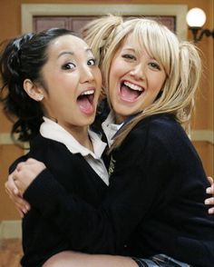 two young women hugging each other in a room with pictures on the wall behind them