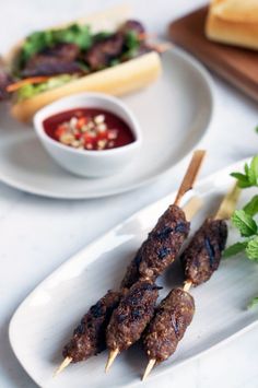 several skewers of food on a plate next to a bowl of dipping sauce