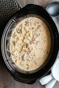 a crock pot filled with soup on top of a wooden table next to spoons