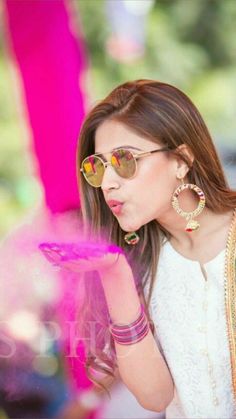 a woman in sunglasses blowing bubbles on her finger