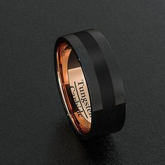 a black and rose gold wedding ring on a black surface with an inscription engraved in the center