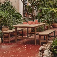 a wooden table with two benches in front of potted plants on the ground and words west elm above it