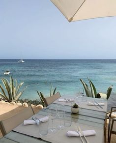 the table is set with wine glasses and place settings for two people on the beach