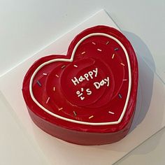 a red heart shaped cake with sprinkles on it's sides and the words happy is day written in white