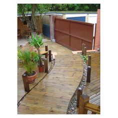 a wooden walkway with potted plants on the side and a garage in the background