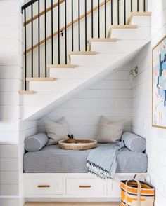 there is a bench under the stairs with pillows on it and a basket in front