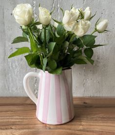 white roses are in a pink and white striped vase