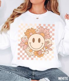 Our retro smiley face graphic sweatshirt features a vintage inspired flower happy face design. You'll love the comfortable material of the Gildan sweatshirt fabric. It ensures a soft and comfortable feel that will keep you feeling good all day long. ✩ Smiley Face Sweatshirt, Flower Shirt, Retro Sweatshirt, Trendy Vintage Crewneck Sweatshirt, Checkered Happy Face, Plus Size Sweatshirt Gift  SIZE UP for an OVERSIZED fit (see size chart in listing photos).  ✩ Our shop uses direct-to-garment printin Retro White Sweatshirt For Spring, Retro Spring Sweatshirt With Graphic Print, Trendy Fall Sweatshirt With Smiley Face, Trendy Smiley Face Sweatshirt For Fall, Fun Graphic Print Sweatshirt For Spring, Spring Graphic Print Fun Sweatshirt, Spring Fun Graphic Print Sweatshirt, White Fun Sweatshirt For Spring, Spring Graphic Print Sweatshirt