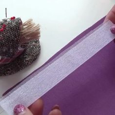 someone is cutting fabric with scissors on a white table and purple material in the background