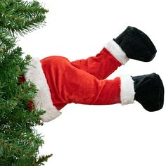 a santa claus costume hanging from a christmas tree with his feet up in the air